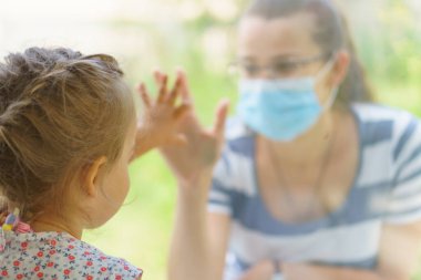 Maskeli Aile Anne ve Kızı. Virüse karşı koruyucu maskelerle pencerenin kenarında oturan mutlu genç bir kadın ve çocuk. Bebek cam üzerinde el ele tutuşuyor. Annem bebek yüzünü okşar.