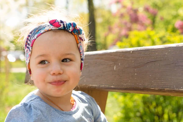 Tijd buiten doorbrengen. Oprechte emoties van een klein meisje. Mooi klein meisje met hoofdband in het voorjaar in het park. close-up uitzicht op kleine meisje die zit op een park bank. — Stockfoto