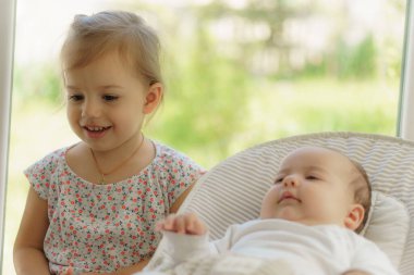 Yeni doğmuş kardeşini öpen tatlı küçük kız. Küçük çocuk yeni doğan kardeşiyle tanışıyor. Beyaz bir fedaide battaniyenin altında uyuyan bir bebek. Çocuklar oynuyor ve kaynaşıyorlar. Küçük yaş farkı olan çocuklar. Yüksek kalite fotoğraf