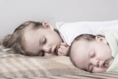 Çocukluk, uyku, rahatlama, aile, yaşam tarzı konsepti. 2 ve 3 yaşlarındaki iki küçük çocuk beyaz ve bej renkli giysiler içinde öğle yemeğinde el ele tutuşarak bej ve beyaz bir yatakta uyurlar.