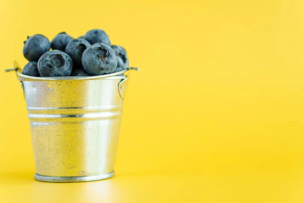 fruits and vegetables, vitamin, healthy food and drink, traditional medicine, gastronomy concept - layout purple blueberry berries in metal bucket with white dot on bright yellow background copy space.