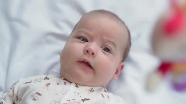 bebeklik, çocukluk, gelişim, tıp ve sağlık konsepti - yeni doğmuş çıplak, uyanık, neşeli bebek buruşuklukları beyaz arka plandaki beşikte uzanan oyuncaklara uzanır