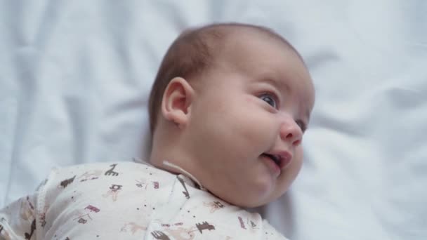 Младенчество, детство, развитие, медицина и концепция здоровья - крупным планом лицо новорожденный голый бодрствующий живой игривый ребенок улыбается и смеется тянется к игрушке лежащей на спине в кроватке на белом фоне — стоковое видео