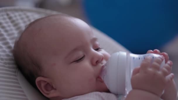 갓난아기의 개월된 아기가 젖병으로 술잔을 마시며 흔들리는 의자에 모습의 — 비디오