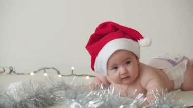 Mutlu noeller ve mutlu yıllar, bebekler, çocukluk, tatil konsepti - yakın plan çıplak bebek Noel Baba şapkalı 6 aylık bebek Noel Baba 'nın karnında Noel ağacı süslemeleri ile sürünüyor.