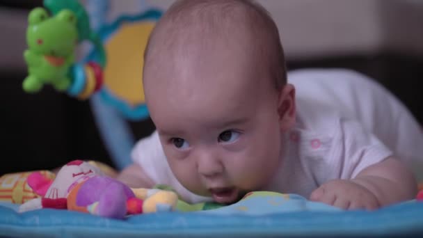 Infancy, childhood, development, summer holiday, lifestyle concept - Close up of happy cute newborn kid 5 month of age laying on floor developing mat Activity Gym baby doing tummy time with toy inside — Stock Video