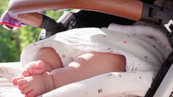 Infância, desenvolvimento, férias de verão, conceito de estilo de vida - bebê close-up em um passeio no verão. Pés minúsculos na criança recém-nascida em carruagem em tempo quente ao ar livre. — Vídeo de Stock