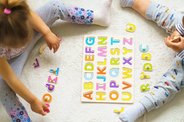 Preparing for school. Preschool education for youngest in kindergartens. Top view of Two little kids makes puzzles out of alphabet on floor at home.Color English Alphabet for children. puzzles on