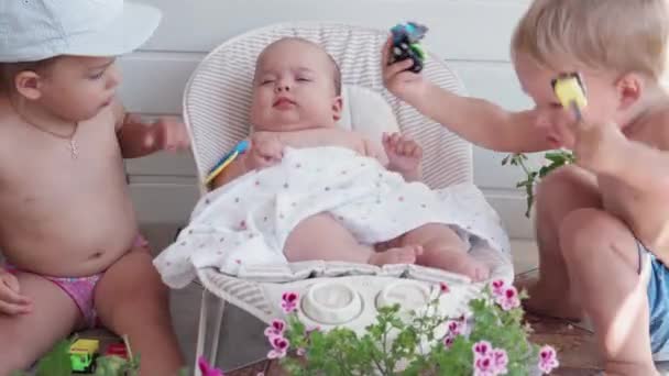 Infancy, childhood, development, summer holiday, medicine and health concept - Close-up top view portrait of newborn baby five months of age lying in rocking chair and two older kids with toy Outside — Stock Video