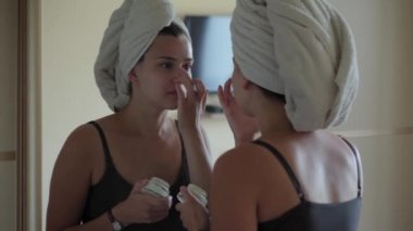 Kadınlar yüzüne krem sürerler. Moda ve güzellik, partiler, kozmetoloji, yaşam tarzı konsepti. Makyaj yapan güzel, koyu renkli, sıradan bir kız yanaklarını kahverengileştirir ve beyaz bir tuğlada tatlı tatlı gülümser.