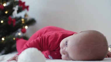 Mutlu Noeller ve mutlu yıllar, bebekler, çocukluk, tatil konsepti - yakın plan 6 aylık Noel Baba şapkalı bebek ve göbeğinde kırmızı tulum Noel ağacında süsleme toplarıyla sürünüyor