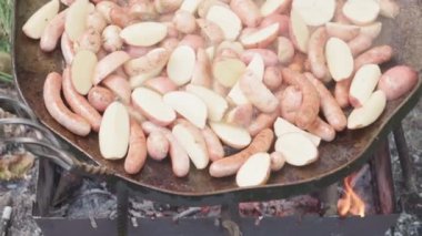 Kafeler ve restoranlar, piknik, doğu mutfağı konsepti - patatesli ve mantarlı yakın çekim sosisler dışarıda kamp ateşi üzerinde yemek pişirmek için büyük kızartma tavasında tütsülenmiş ve kızartılmış kömürlerde kızartılmış..
