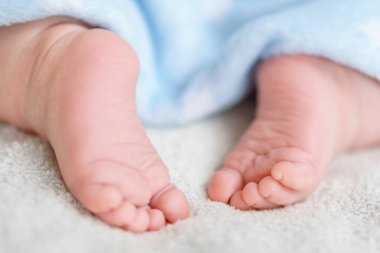Mavi, yumuşak, sıcak bir battaniyeyle kaplanmış küçük çıplak bacaklar ve yeni doğmuş ayaklar. Küçük bebek yatakta beyaz battaniyenin üzerinde uyur. Dermatoloji, pediatri, masumiyet, çocukluk, annelik kavramları. Soace kopyala