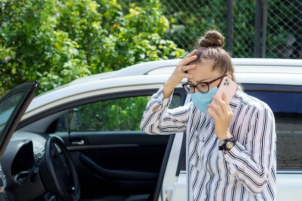 young business lady speaks on phone wearing a medical mask inform about car accident. Telephone conversation about the tragedy at distance during quarantine period. Negative emotions of fear anxiety.