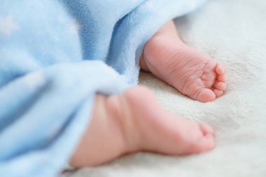 Mavi, yumuşak, sıcak bir battaniyeyle kaplanmış küçük çıplak bacaklar ve yeni doğmuş ayaklar. Küçük bebek yatakta beyaz battaniyenin üzerinde uyur. Dermatoloji, pediatri, masumiyet, çocukluk, annelik kavramları. Anlaşıldı Soace. Yüksek kalite fotoğraf