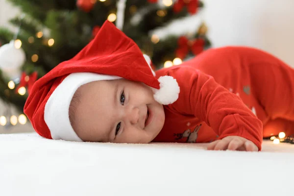 Wesołych Świąt Bożego Narodzenia i szczęśliwego Nowego Roku, niemowlęta, dzieciństwo, koncepcja świąt - zbliżenie nagie 6 miesięcy noworodka w kapeluszu Świętego Mikołaja na brzuchu roi się od dekoracji na choince. — Zdjęcie stockowe
