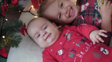 Mutlu Noeller ve mutlu yıllar, bebek, çocukluk, tatil konsepti - yakın plan 6 aylık Noel Baba şapkalı bebek ve ablasıyla kırmızı tulum Noel ağacının yanında toplarla yatıyordu.