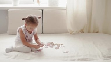 Aile, bebek, eğitim, zihinsel gelişim kavramları. Üç yaşında tatlı bir kız evdeki karantinadaki parlak güneşli çocuk odasında beyaz yatakta bulmaca çözüyor. Çocuk kapalı alanda kendini öğrenmekle meşgul.