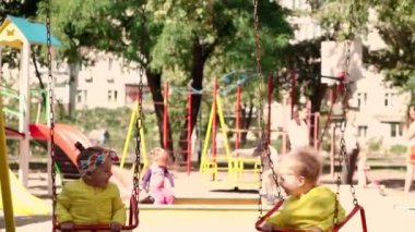 çocukluk, oyun, eğlence, dostluk, yaşam tarzı konsepti - sarı ceketli iki anaokulu çocuğunun genel planı 2 ve 3 yaşındaki tatlı gülümseme neşeyle salıncakta sallanıyor