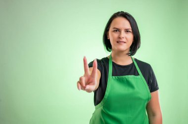 Yeşil önlüklü ve siyah tişörtlü kadın aşçı, yeşil arka planda izole edilmiş zaferi gösteriyor.