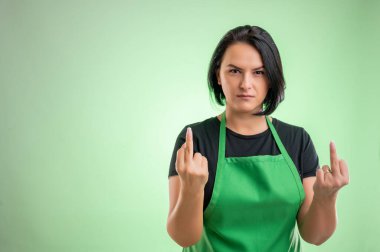 Female cook with green apron and black t-shirt, showing double fuck you isolated on green background