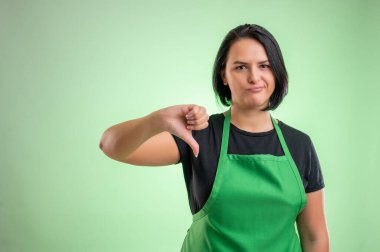 Yeşil önlüklü ve siyah tişörtlü kadın aşçı, yeşil arka planda izole edilmişlerden hoşlanmadığını gösteriyor.