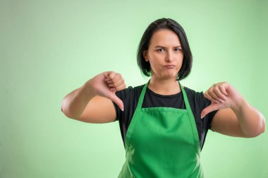Yeşil önlüklü ve siyah tişörtlü kadın aşçı, yeşil arka planda çifte hoşnutsuzluk gösteriyor.