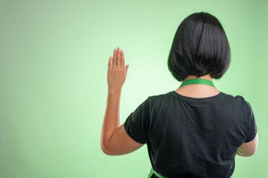 Yeşil önlüklü ve siyah tişörtlü kadın aşçı, yeşil arka planda izole edilmiş bir şekilde yemin ediyor.