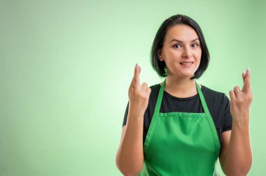 Yeşil önlüklü ve siyah tişörtlü kadın aşçı, yeşil arka planda çifte şans gösteriyor.