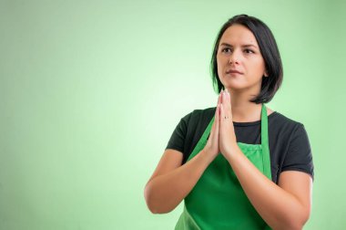 Yeşil önlüklü ve siyah tişörtlü kadın aşçı yeşil arka planda yalnız dua ediyor.