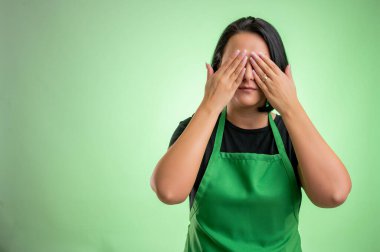 Yeşil önlüklü ve siyah tişörtlü kadın aşçı, yeşil arka planda izole edilmiş kör bir kavram gibi gözü örtüyor.