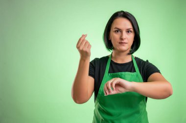 Yeşil önlüklü ve siyah tişörtlü kadın aşçı, zamanın yeşil arka planda izole edilmiş para olduğunu gösteriyor.