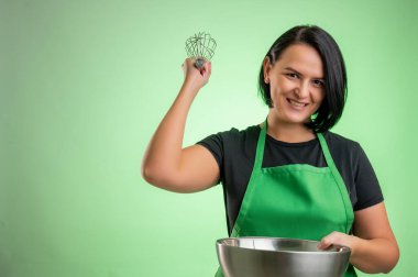 Yeşil önlüklü ve siyah tişörtlü kadın aşçı, kaseyi tut ve yeşil arka planda izole edilmiş olarak ellerini çırp.