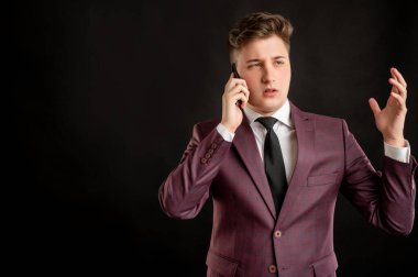 Sarı saçlı, bordo ceketli, beyaz gömlekli, siyah kravatlı hoşnutsuz bir yüz ve jestler takmış ve cep telefonuyla fotokopi çekilen siyah arka planda poz veren bir hukuk öğrencisi.