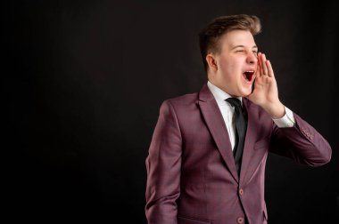 Sarı saçlı, bordo ceketli, beyaz gömlekli ve siyah kravatlı bir hukuk öğrencisi elini ağzına sokup fotokopi çekilen siyah arka planda poz veriyor.