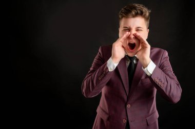 Sarı saçlı, bordo ceketli, beyaz gömlekli ve siyah kravatlı bir hukuk öğrencisi elleri ağzında bağırıyor. Fotokopi çekilen siyah arka planda poz veriyor.