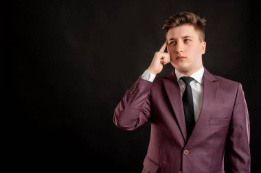 Sarı saçlı, bordo ceketli, beyaz gömlekli ve siyah kravatlı bir hukuk öğrencisi, fotokopi alanındaki siyah arka planda poz veriyor.