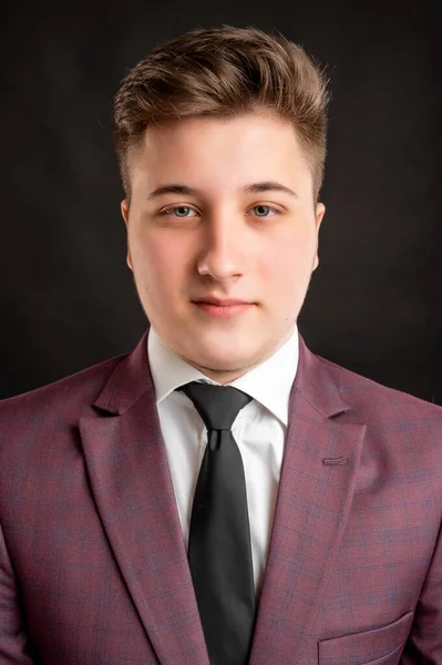 Portrait of law student with blond hair dressed in burgundy jacket, white shirt and black tie posing on isolated background with copy space advertising area