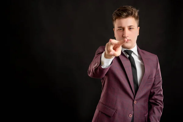 Law student with blond hair dressed in burgundy jacket, white shirt and black tie doing I am watching you gesture posing on isolated black background with copy space advertising area