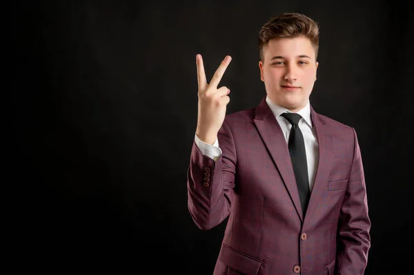 Law student with blond hair dressed in burgundy jacket, white shirt and black tie counting two with his finger posing on isolated black background with copy space advertising area