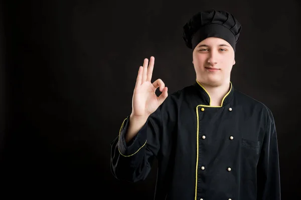 Portret Młodego Mężczyzny Ubranego Czarny Kombinezon Kucharski Pokazujący Znak Pozujący — Zdjęcie stockowe