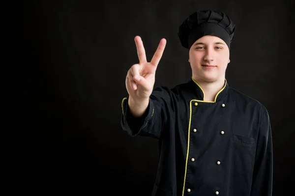 Mladý Muž Oblečený Černém Kuchař Oblek Ukazuje Vítězství Znamení Pózování — Stock fotografie