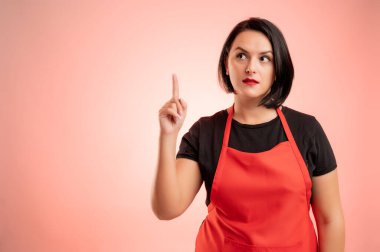 Markette çalışan kırmızı önlüklü ve siyah tişörtlü kadının kırmızı arka planda izole edilmiş iyi bir fikri var.