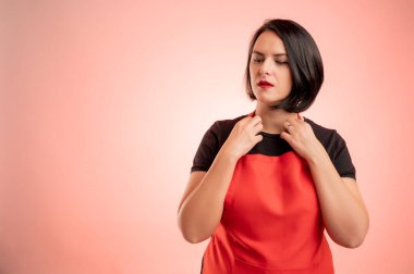 Markette çalışan kırmızı önlüklü ve siyah tişörtlü bir kadın. Yakasını kırmızı arka planda izole etmiş.