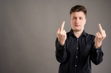 Gri arka planda çift müstehcen hareketler gösteren, günlük siyah gömlekli, şık ve çekici bir adamın portresi.