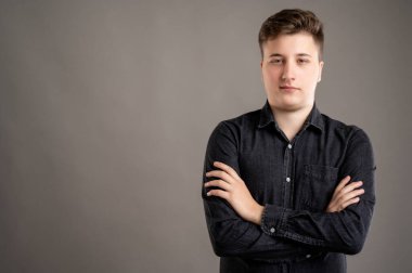 Siyah gömlekli, ciddi ve şık bir erkeğin portresi kolları çapraz duran gri arka planda fotokopi alanı reklam alanı ile izole edilmiş.