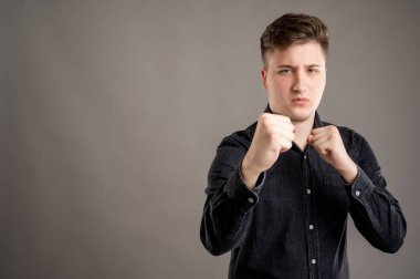 Gri arka planda izole edilmiş fotokopi alanı reklam alanı ile dövüşmek gibi yumrukları olan ciddi, şık, çekici bir adamın portresi.