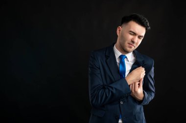 Mavi takım elbiseli bir iş adamı portresi ve eli göğsünde akut ağrıdan muzdarip siyah arka planda izole edilmiş fotokopi alanı reklam alanı olan bir kravat.