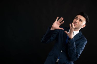 Mavi takım elbiseli ve kravatlı bir iş adamı portresi siyah arka planda izole edilmiş, fotokopi alanı reklam alanında korkunç bir jest yapıyor.