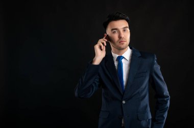 İş adamının mavi takım elbiseli ve kravatlı portresi. Telefonda konuşuyor. Siyah arka planda, fotokopi alanı reklam alanında.